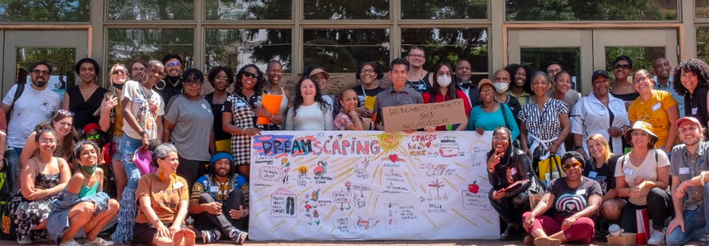 A large group of people pose for a photo outside of a building. A large chart that says "Dreamscaping" sits in the middle of the group.