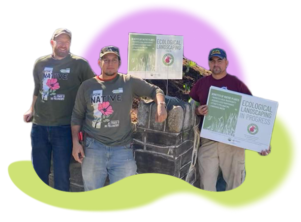 A photograh of worker owners of Swamp Rose Co-op. They stand by some supplies while wearing t-shirts highlighting native plants and holding signs about ecological landscaping.