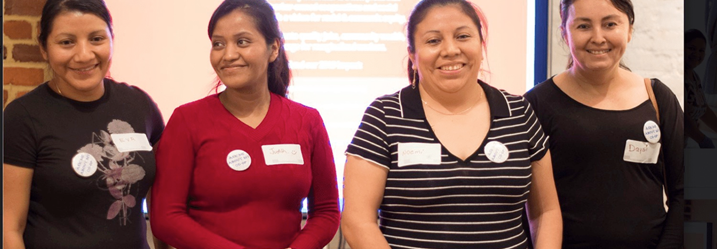 Worker owners of Dulce Hogar smiling at the camera during a presentation in front of a room.