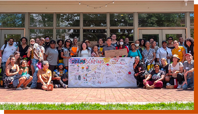 A large group of people pose for a photo outside of a building. A large chart that says "Dreamscaping" sits in the middle of the group.