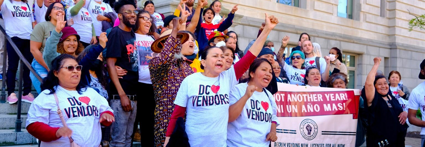 Street vendors rally together on the steps of a building. Many wear shirts that read "DC Loves Vendors."
